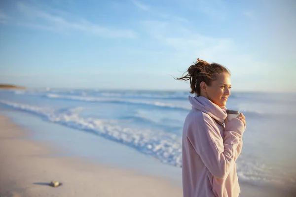 傍晚时分 穿着舒适的毛衣 在海滩边喝咖啡的悠闲的时髦女人 — 图库照片