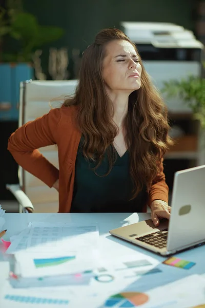 悲しいトレンディーな40歳の中小企業経営者の女性ラップトップと現代の緑のオフィスで腰痛 — ストック写真