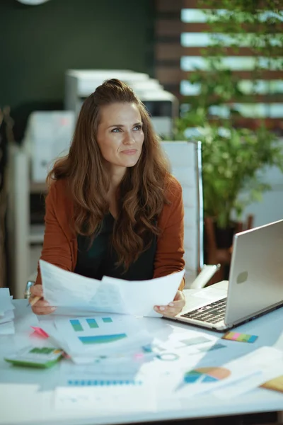 現代のグリーンオフィスで書類を扱うノートパソコンを持つトレンディーな中小企業経営者の女性を笑顔 — ストック写真