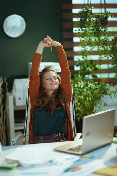 リラックスした現代的な中年中小企業の所有者女性とラップトップストレッチで現代的な緑のオフィス — ストック写真