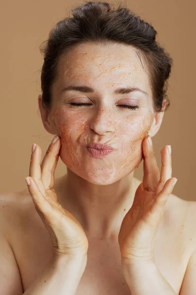 young 40 years old woman with face scrub isolated on beige background.