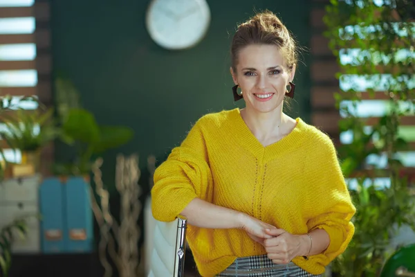現代の緑のオフィスに立って黄色のセーターで流行の中小企業の所有者の女性を笑顔 — ストック写真