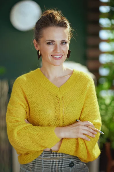 現代の緑のオフィスに立つ黄色のセーターに身を包んだ40歳の中小企業経営者の女性の肖像 — ストック写真