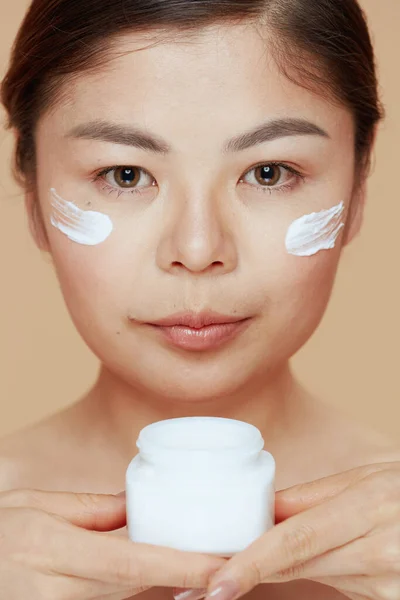 Moderne Frau Mit Gesichtscremeglas Und Gesichtscreme Auf Beigem Hintergrund — Stockfoto