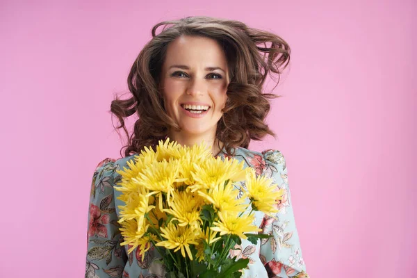 黄色の菊の花がピンクの背景にジャンプと長い波状ブルネットの髪を持つ流行の女性を笑顔 — ストック写真