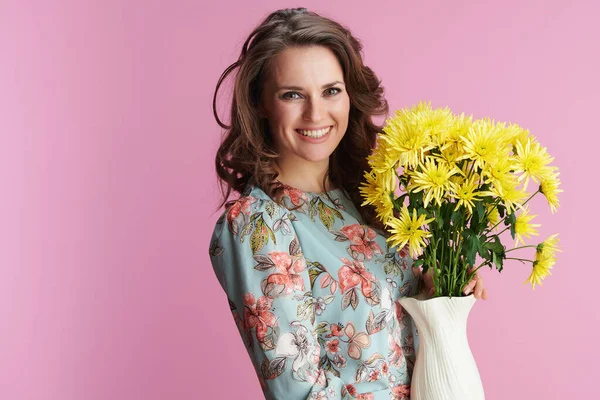 ピンク色に隔離された花瓶に黄色の菊の花と花のドレスで幸せな現代女性の肖像画 — ストック写真