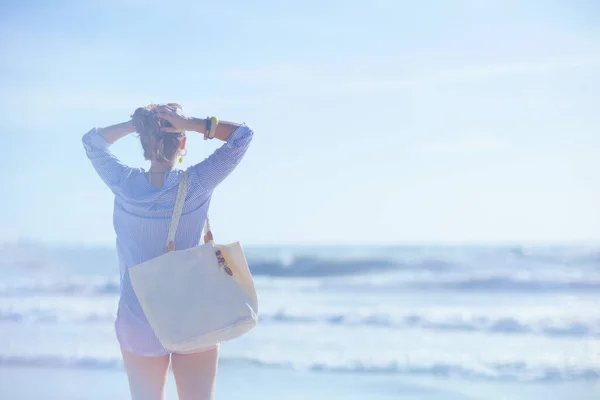 在海滩上看到从后面的女人手里拿着白色草袋放松一下 — 图库照片