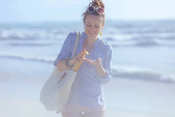 40歳の女性が笑顔でビーチでSpfと白のストローバッグを着て — ストック写真