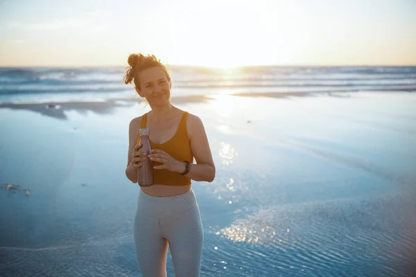 Lächelnde Joggerin Fitnesskleidung Mit Wasserflasche Abend Strand — Stockfoto