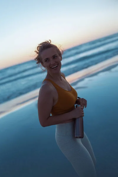 Lächelnde Fitte Joggerin Sportkleidung Mit Wasserflasche Strand Bei Sonnenuntergang — Stockfoto
