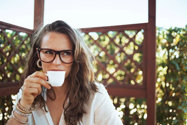 穿着白衬衫 戴着眼镜的快乐中年妇女在院子里喝咖啡 — 图库照片