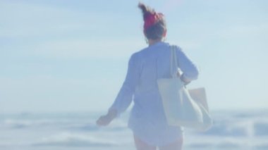 Beyaz saman çantalı orta yaşlı bir kadın kumsalda neşe içinde bekliyor..