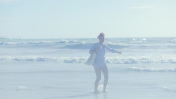 从后面看到一个女人拿着白色的草袋在海滩上欢欣鼓舞 — 图库视频影像