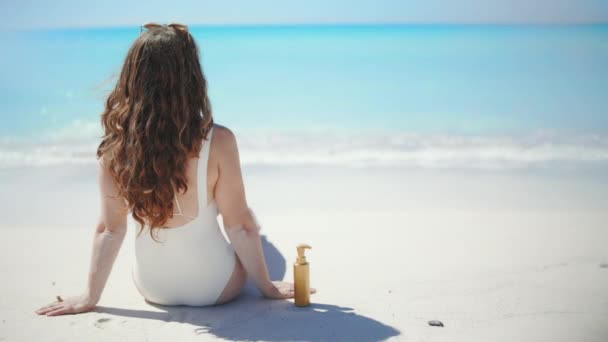 穿着白色泳衣坐在海滩上笑着的40岁的现代女人 — 图库视频影像