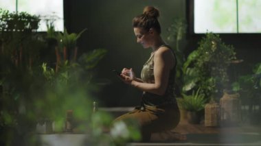 stylish female in the modern green living room doing yoga and using smartphone.