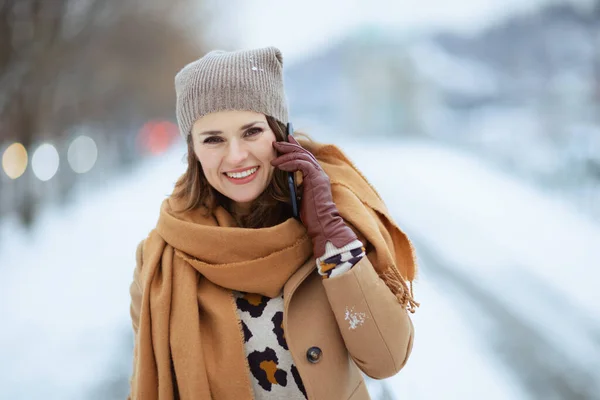 40歳のスタイリッシュな茶色の帽子の女性と冬に街の外でスマートフォンを使用して手袋でラクダのコートのスカーフ — ストック写真
