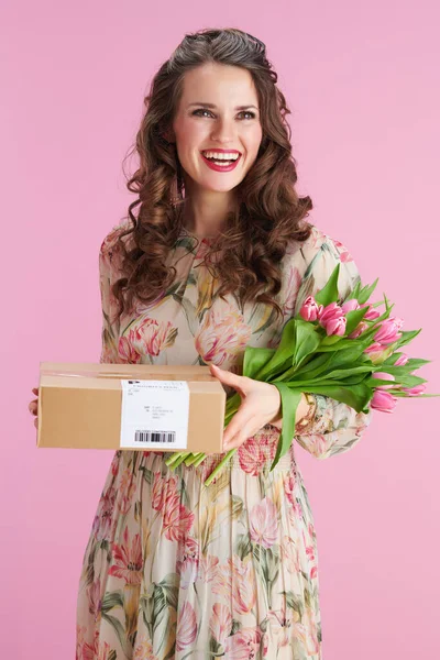 笑顔40歳の女性とともに長い波状ブルネット髪とともにチューリップ花束と小包に対してピンクの背景 — ストック写真