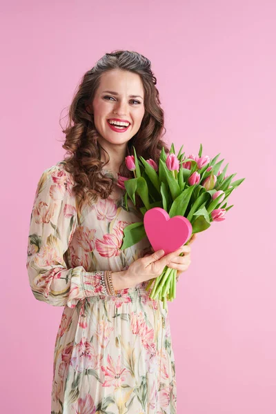 幸せなスタイリッシュな女性とともに長い波状ブルネットの髪でチューリップ花束とピンクの心はピンクの上に隔離 — ストック写真
