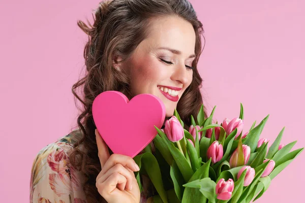 ピンク色に孤立したチューリップの花束とピンクのハートを持つ花のドレスのエレガントな女性を笑顔 — ストック写真