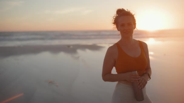 フィットネスの女性のジョガーは夜にビーチで水のボトルとフィットネス服を着て — ストック動画