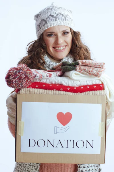 Hello winter. happy modern 40 years old woman in sweater, mittens, hat and scarf against white background with donation box.