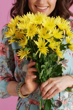 Uzun dalgalı esmer saçlı, sarı kasımpatı çiçekli, pembe renkli gülümseyen kadına yakın çekim..