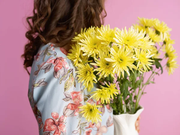若いです女性とともに長い波状ブルネット髪とともに黄色菊の花で花瓶にピンクの背景 — ストック写真