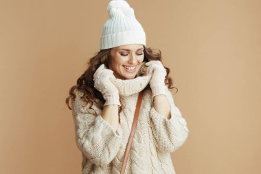 Merhaba kış. Bej renkli kazak, eldiven ve bej bir yakaya sarılı şapka giyen gülümseyen modern bir kadın..