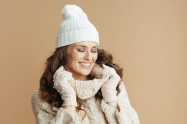 Merhaba kış. Bej süveter, eldiven ve bej arka planda şapka giyen zarif bir kadın..