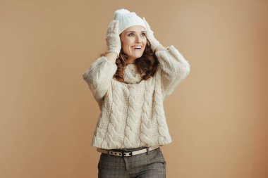 Merhaba kış. Bej süveter, eldiven ve bej arka planda şapka giyen zarif bir kadın..