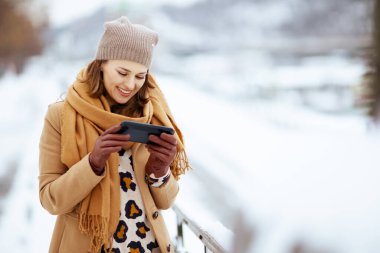 Kahverengi şapkalı, deve ceketli, eldivenli, şık bir kadın kışın şehrin dışındaki akıllı telefondan mesaj yolluyor..