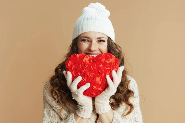 幸せなエレガントな女性でベージュのセーター ミトンと帽子でベージュの背景に対して赤いハート — ストック写真