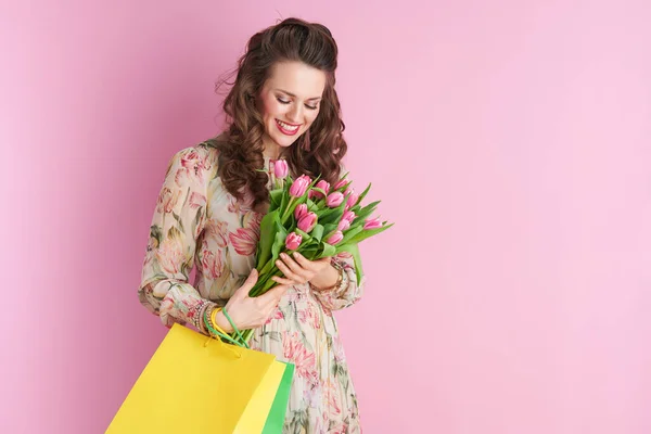 幸せな現代女性で花のドレスでチューリップ花束とショッピングバッグ隔離されたピンク — ストック写真