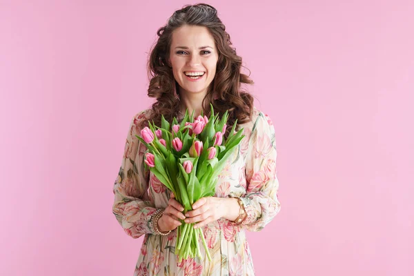 幸せな現代的な中年女性で花のドレスとともにチューリップ花束隔離されたピンク — ストック写真