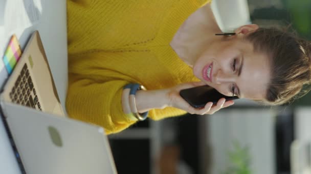 幸せなトレンディーな中年中小企業の所有者女性で黄色のセーターとノートパソコンの話で現代の緑のオフィスのスマートフォン — ストック動画