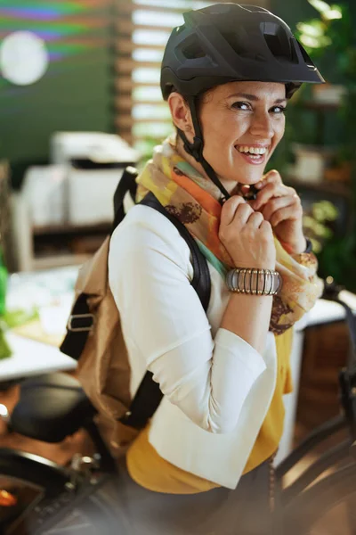 happy stylish business woman in bike helmet with bike and backpack in modern eco office.