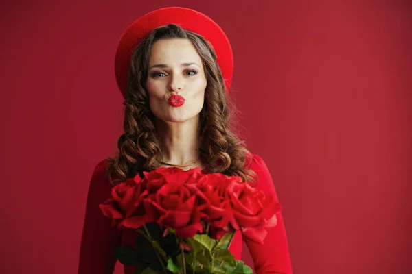 stock image Happy Valentine. modern woman in red dress and beret isolated on red background with red roses sending a kiss.