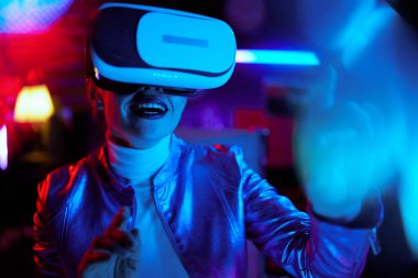 Neon metaverse futuristic concept. happy modern woman in vr headset using virtual reality technology in modern office.