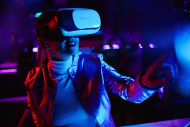 Neon metaverse futuristic concept. elegant middle aged woman in virtual reality goggles exploring metaverse in modern office.