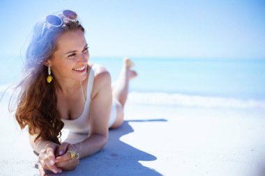 happy elegant female in white swimsuit laying at the beach.