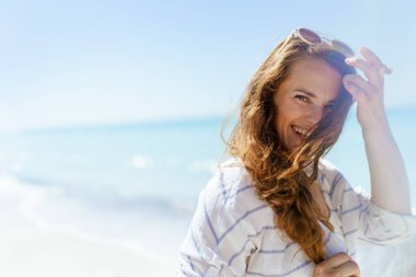 Portrait of happy modern woman at the beach adjusting hair.