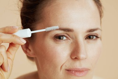 Closeup on young female with brow brush on beige background.