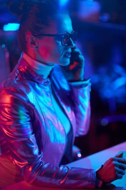 Neon metaverse futuristic concept. stylish woman in glasses speaking on a smartphone in modern office.