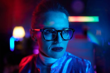 Neon metaverse futuristic concept. Portrait of pensive trendy woman in glasses in modern office.