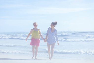 Full length portrait of smiling modern mother and teenage daughter at the beach walking.