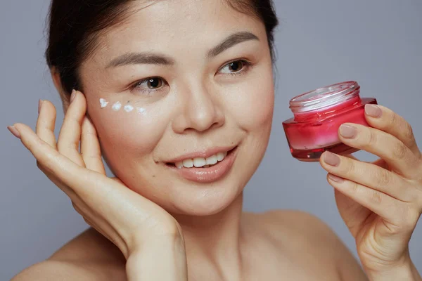 modern asian woman with facial cream jar and facial cream on face on blue background.