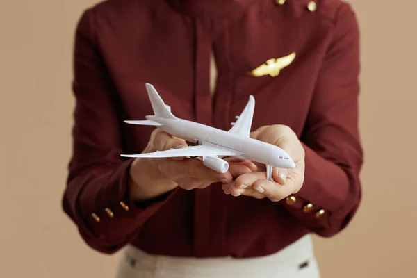 Closeup on female air hostess on beige background with a little airplane.