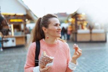 Easter fun. modern middle aged woman in pink blouse at the fair in the city eating trdelnik.
