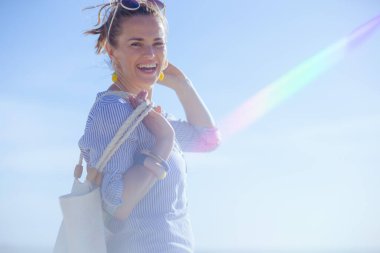 Portrait of happy elegant 40 years old woman with white straw bag at the beach.
