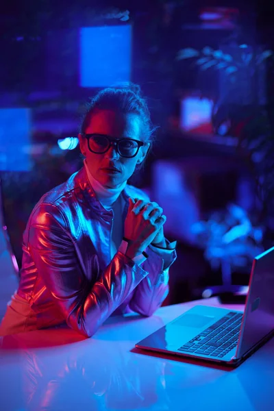 Neon metaverse futuristic concept. pensive elegant woman in glasses using laptop in modern office.